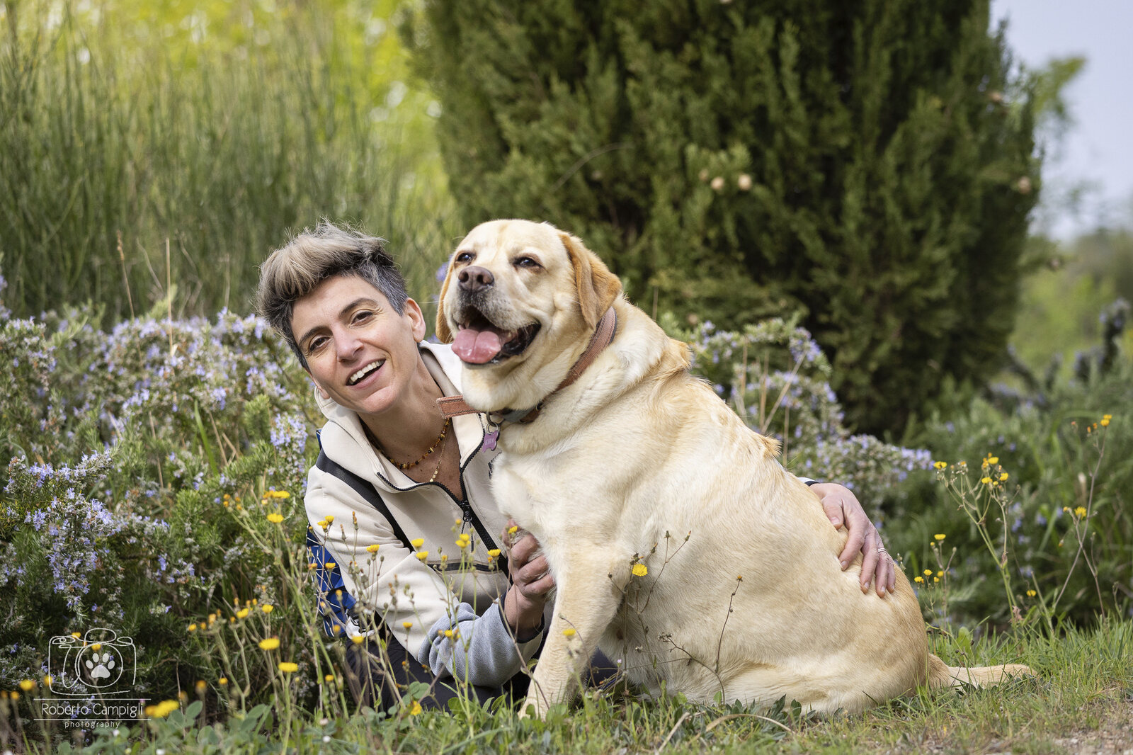 Una persona abbraccia il proprio Labrador in un prato fiorito